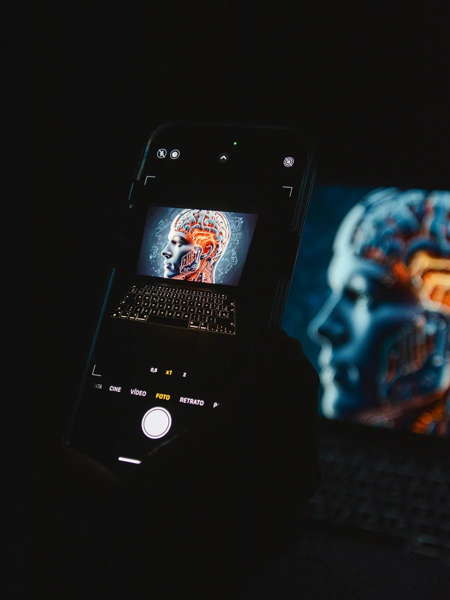 Retrato de un teléfono inteligente capturando una imagen digital de un cerebro tecnológico en una pantalla, destacando soluciones de inteligencia artificial y tecnología avanzada en un entorno oscuro.