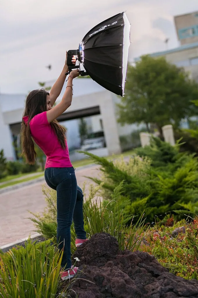 Mujer joven sonriendo usando equipo de iluminación profesional en exteriores, promoviendo soluciones de tecnología e innovación para negocios digitales.
